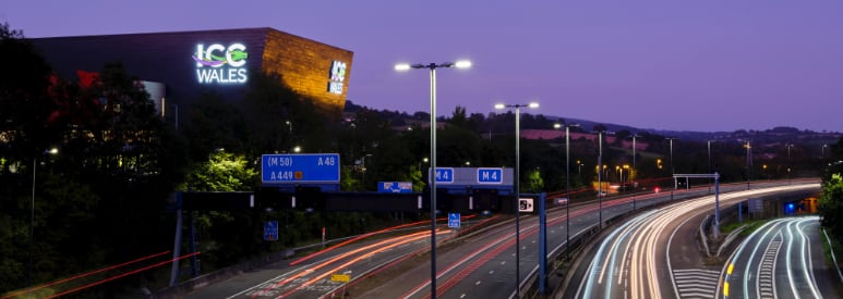An exterior photo of the Wales International Convention Centre at night with motorway lights in the foreground